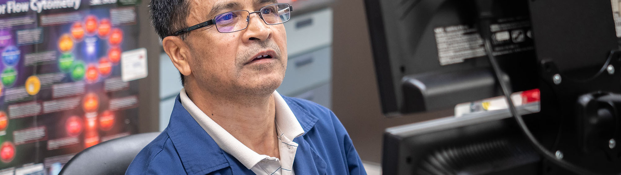 man in blue lab coat watching monitor screen